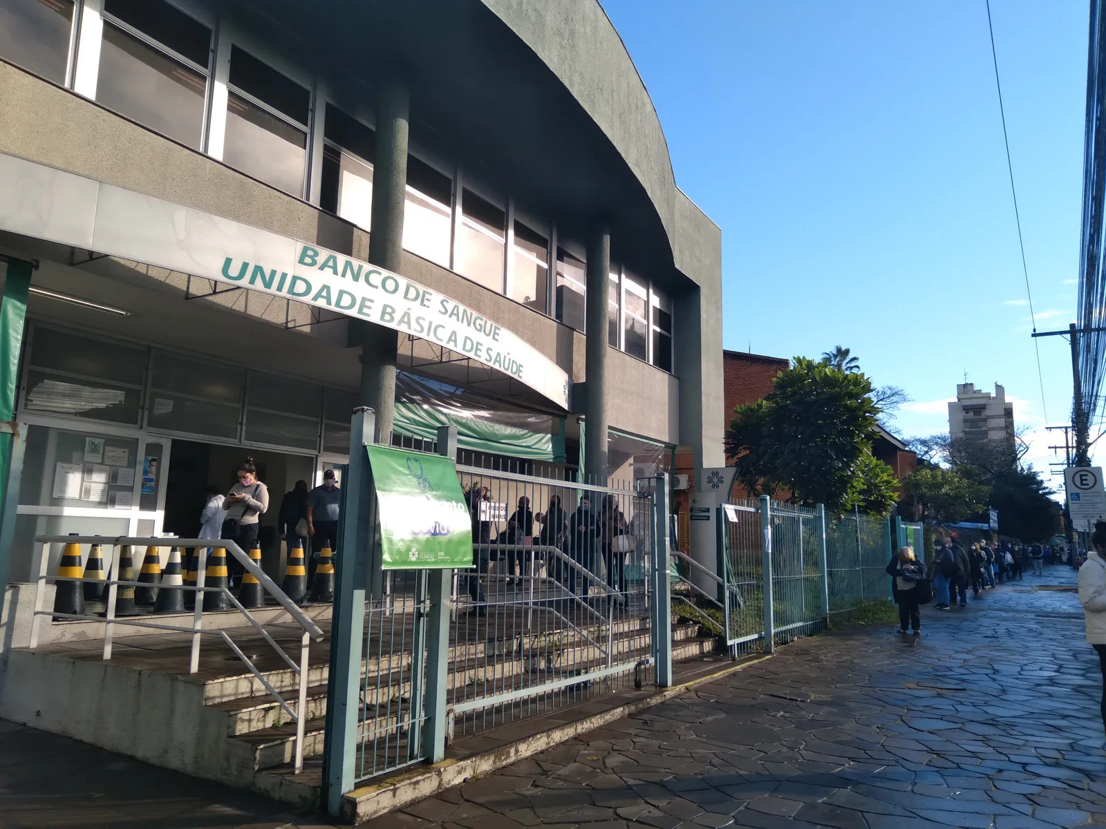 Entrada da Unidade Básica de Saúde Santa Cecília, em Porto Alegre, com pessoas junto ao acesso
