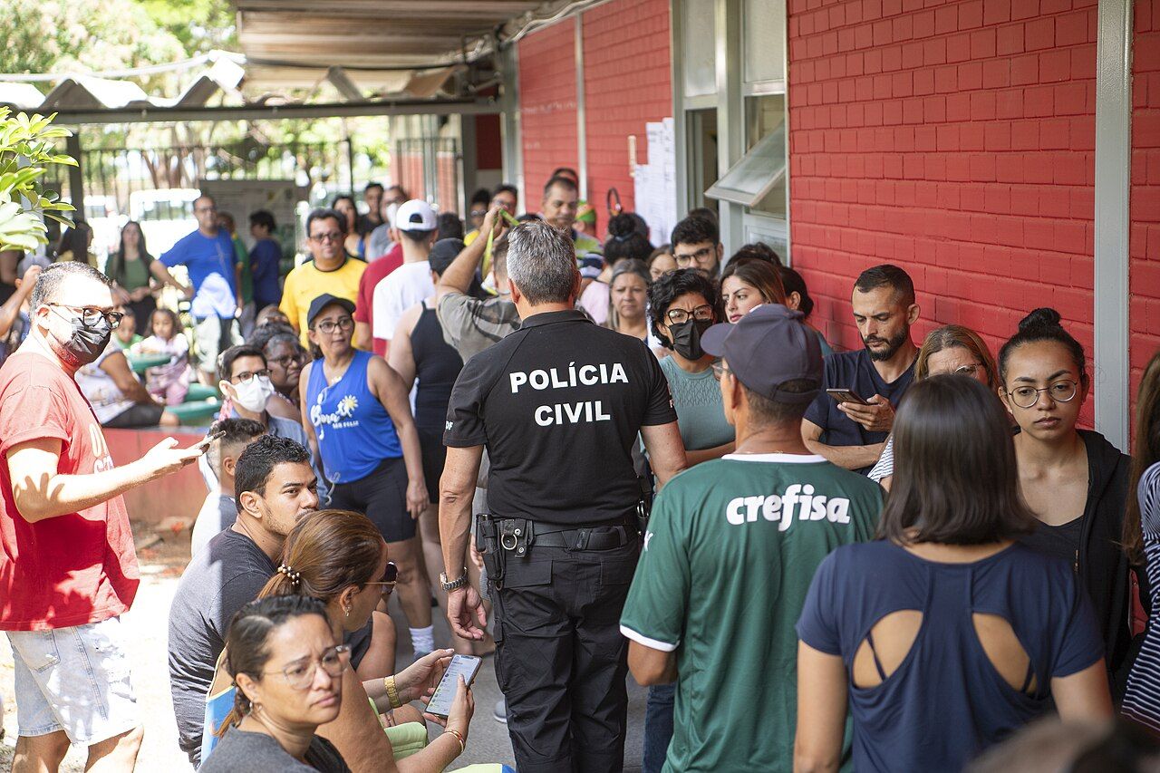 Eleitores em corredor de local de votação e policial civil ao centro, em registro de 2022.