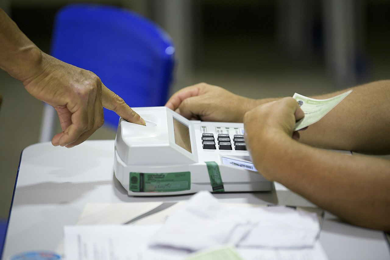 Mesário aponta o leitor biométrico enquanto eleitor posiciona o dedo no terminal da seção eleitoral