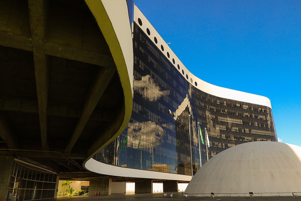 Fachada curva e envidraçada da sede do Tribunal Superior Eleitoral em Brasília, ao lado de uma cúpula branca