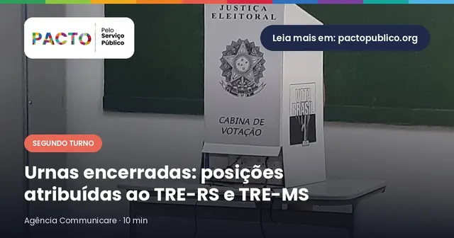 Cabine de votação de papelão da Justiça Eleitoral sobre uma mesa, diante de um quadro verde de sala de aula